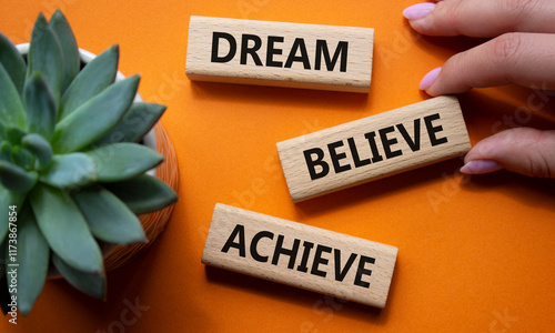 Dream Believe Achieve symbol. Wooden blocks with words Dream Believe Achieve. Businessman hand. Beautiful orange background with succulent plant photo