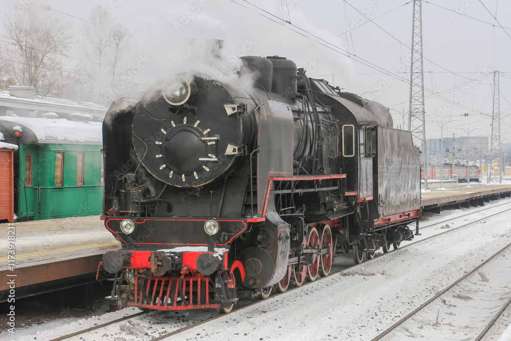 Obraz premium An old steam locomotive in clouds of smoke near a railway station platform