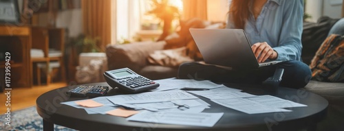 Stressed young Asian man analyzing financial documents in home office, calculating expenses on laptop with bills and calculator on coffee table photo