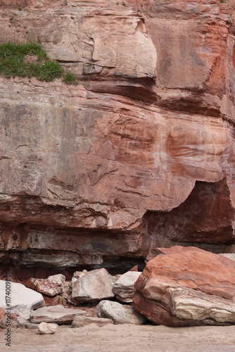 Sandy Red Rock Cliff Face Crumbled onto Beach.