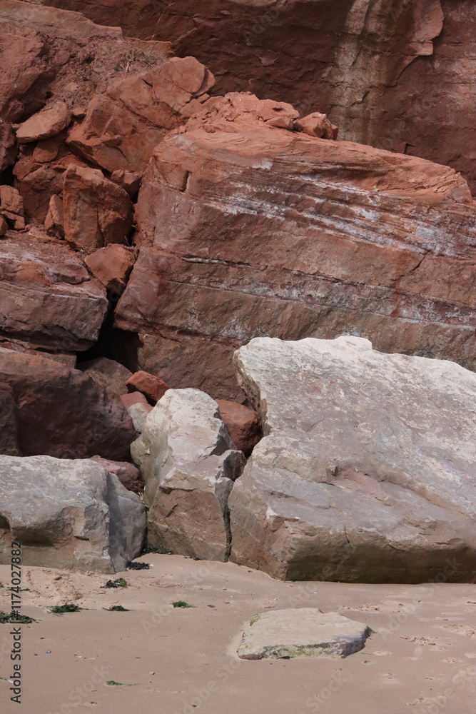 Naklejka premium Crumbled Red Rocks Sliding onto Sandy English Beach
