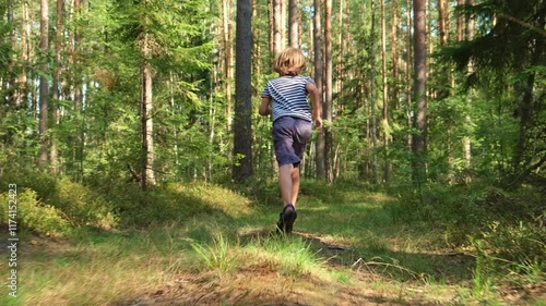 Little boy in striped t-shirt, shorts and sandals running away from persecutor in the woods. Teen running in the forest. Back rear following cinematic shot view. Chase in park, chasing a child photo