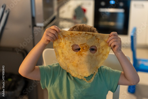Cheerful boy celebrating Maslenitsa with creative pancake mask