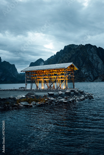 An Enchanting Illuminated Wooden Structure Situated by the Water Beneath a Beautifully Cloudy Sky photo