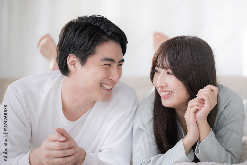 Smiling, staring couple lying on bed in bedroom, relaxing on their stomachs. Smiling, staring couple lying on bed in bedroom, relaxing on their stomachs.