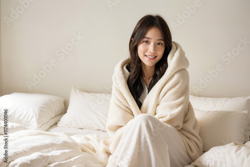 A woman is sitting on a bed with a white blanket wrapped around her