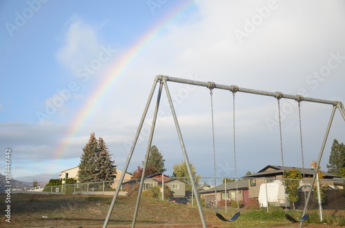 Parque infantil en un día soleado, con columpios en primer plano y un colorido arcoíris en el cielo, creando una escena alegre y vibrante de diversión al aire libre. photo