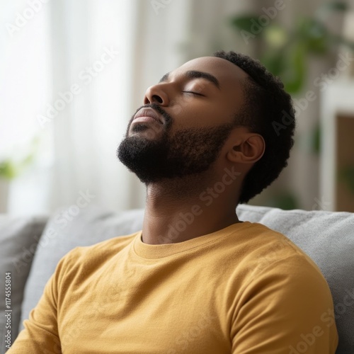A man in a yellow shirt relaxes on a couch, eyes closed, enjoying a moment of peace.