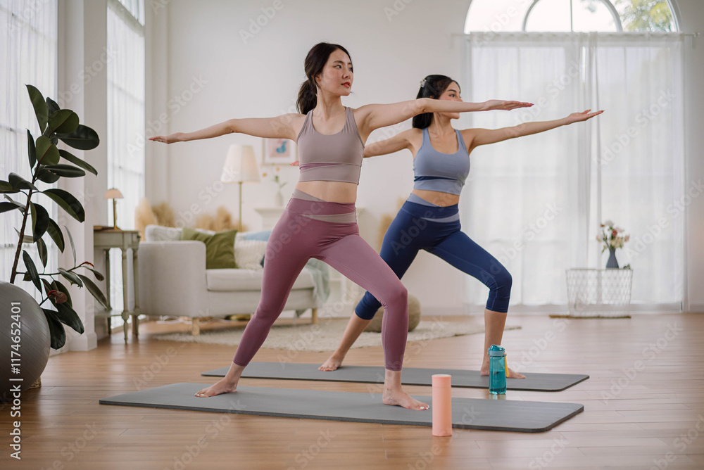 Obraz premium Two Asian woman wearing sportwear practicing yoga at home studio. Couple females exercising with yoga for flexibility body in living room. Health care and wellness activities.