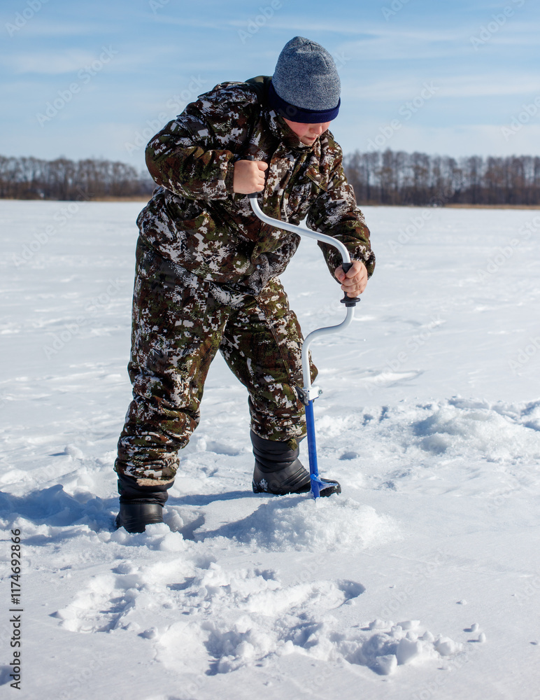 A man in camouflage clothing is standing in the snow with a blue ice auger A man in camouflage clothing is standing in the snow with a blue ice auger