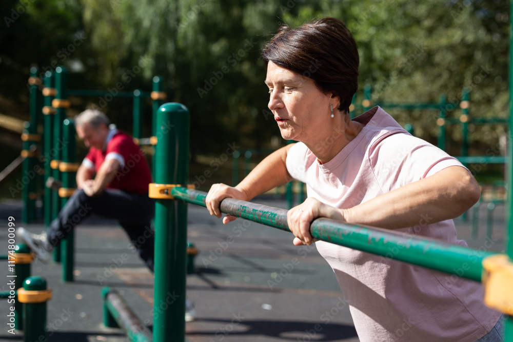 Fototapeta premium Mature woman doing push-ups from the crossbar on outdoor sports ground