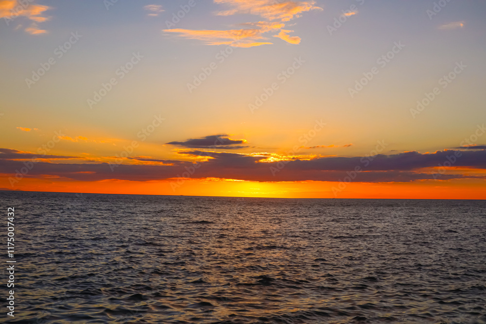 Fototapeta premium Landscape A breathtaking sunset paints the sky with hues of orange and yellow, casting a warm glow on the calm ocean and the rocky shoreline. (3)
