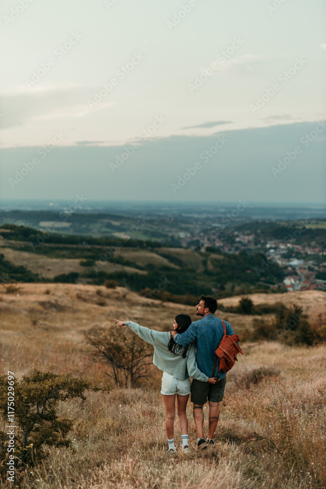Fototapeta premium Couple walking through tall grass, enjoying a sunset in nature. A man carrying a backpack and holding his partner's hand