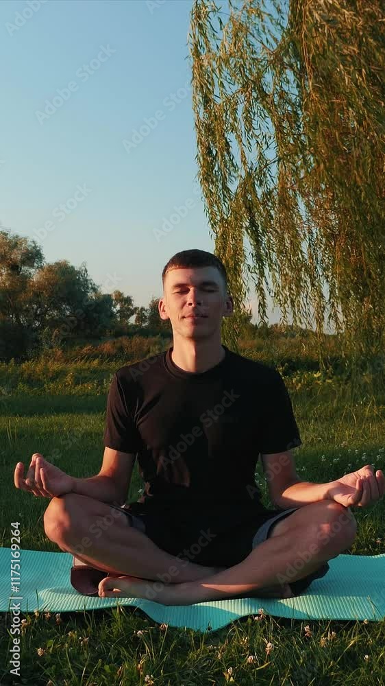 Man practicing yoga exercises on fitness mat at park in morning. Vertical video