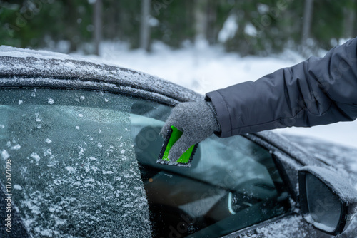 Removing frost from car window with green scraper in winter scene.	
 photo