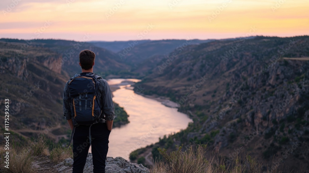 Fototapeta premium Hiking adventure man stands on mountain overlooking river at sunset