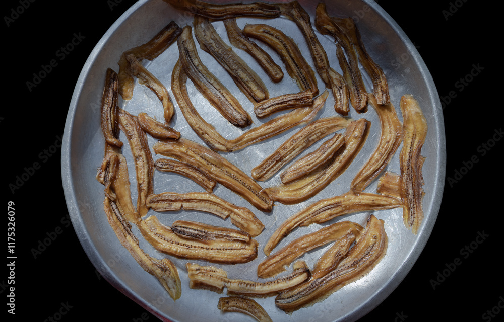 Top view of Natural Dehydrated Bananas on steel round tray with Black background. Delicious sun-dried Sliced Banana, Top view, use it as your Wallpaper, Poster and Space for text, Selective focus.