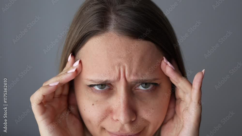 Young caucasian woman touching the forehead showing active facial expressions on her face by raising and lowering her eyebrows on a dark grey background. Wrinkling the forehead. Skin care. Close up Young caucasian woman touching the forehead showing active facial expressions on her face by raising and lowering her eyebrows on a dark grey background. Wrinkling the forehead. Skin care. Close up