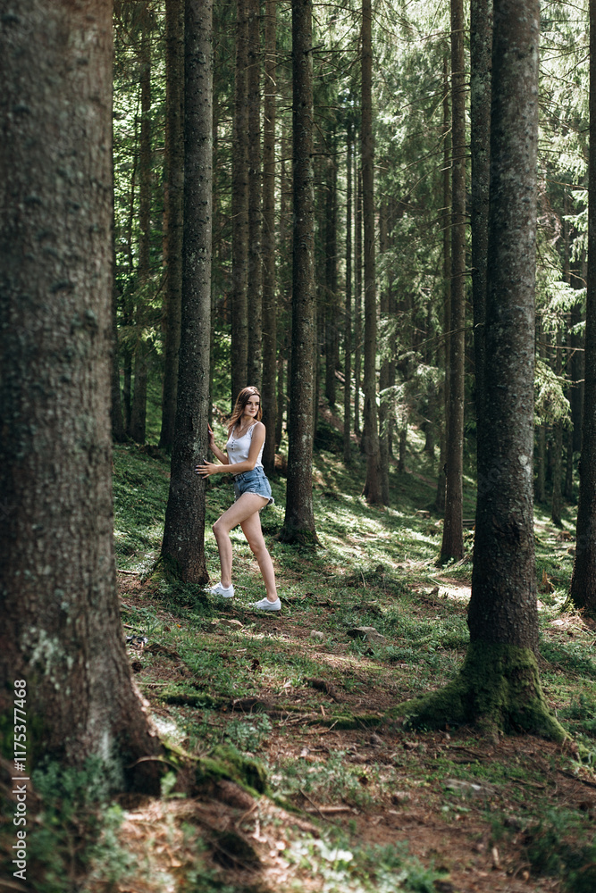 a forest with tall trees, between which a girl walks. She stands with her back to the camera, arms outstretched. She is wearing a white T-shirt and short denim shorts. a forest with tall trees, between which a girl walks. She stands with her back to the camera, arms outstretched. She is wearing a white T-shirt and short denim shorts.