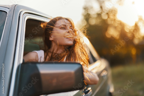 Young woman enjoying a summer road trip, with wind in her hair and a joyful expression, captured in soft golden light during sunset. photo