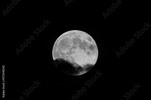 Close-up photo of the moon partially covered by clouds. Moon photo with black background. Cloudy photo of the moon.
