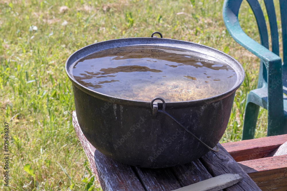 A large metal pot full of water placed on a wooden bench on a green lawn. A large metal pot full of water placed on a wooden bench on a green lawn.