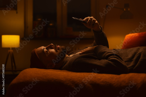 A man lying on a bed holding a phone watching.