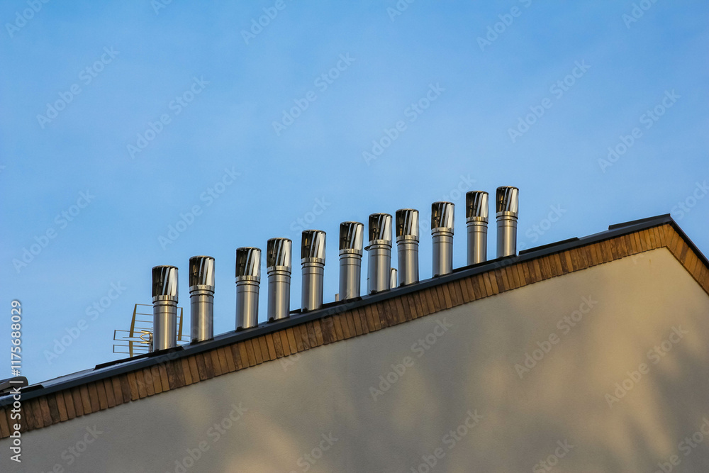Factory rooftop with multiple metal chimneys under clear blue sky Factory rooftop with multiple metal chimneys under clear blue sky
