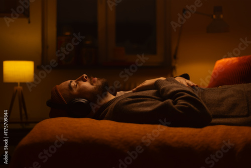 A man lying on a bed wearing wireless headphones listening.