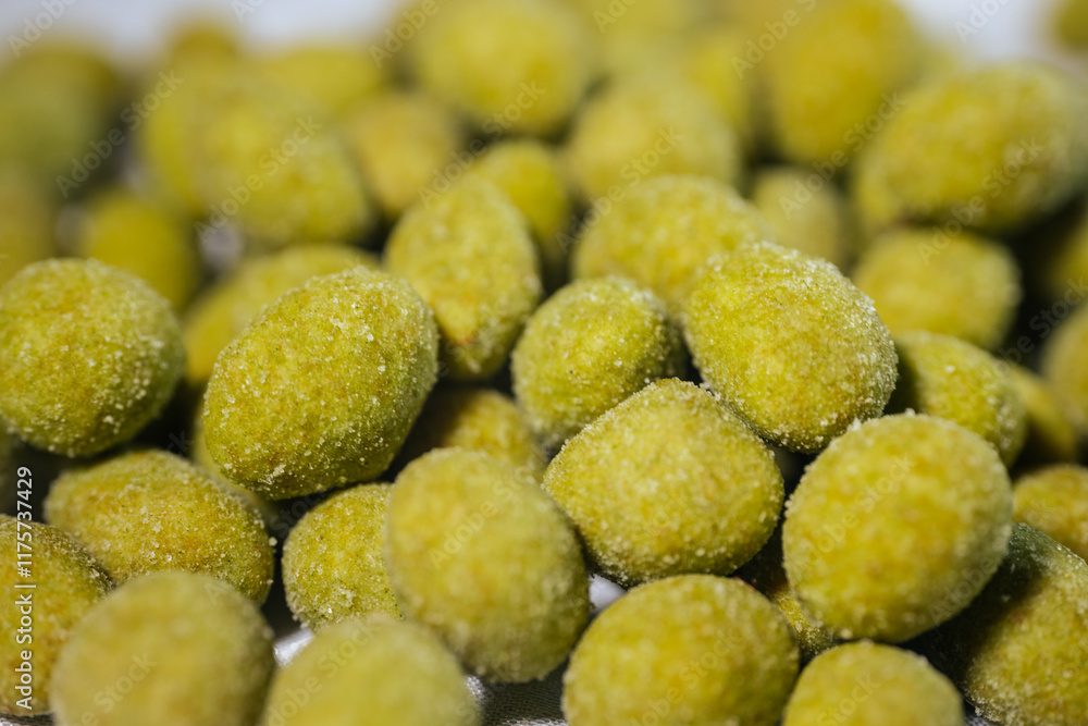 A close-up view of bright yellow-green wasabi-flavored nuts coated in a fine powder, creating a spicy and crunchy snack. Blurred background for emphasis. A close-up view of bright yellow-green wasabi-flavored nuts coated in a fine powder, creating a spicy and crunchy snack. Blurred background for emphasis.