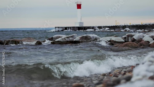 Wallpaper Mural A stunning winter scene: a lighthouse stands amidst icy rocks and snow. Waves crash against the shore, blending water and foam, while the wind adds drama. Frozen beauty captures the essence of winte Torontodigital.ca