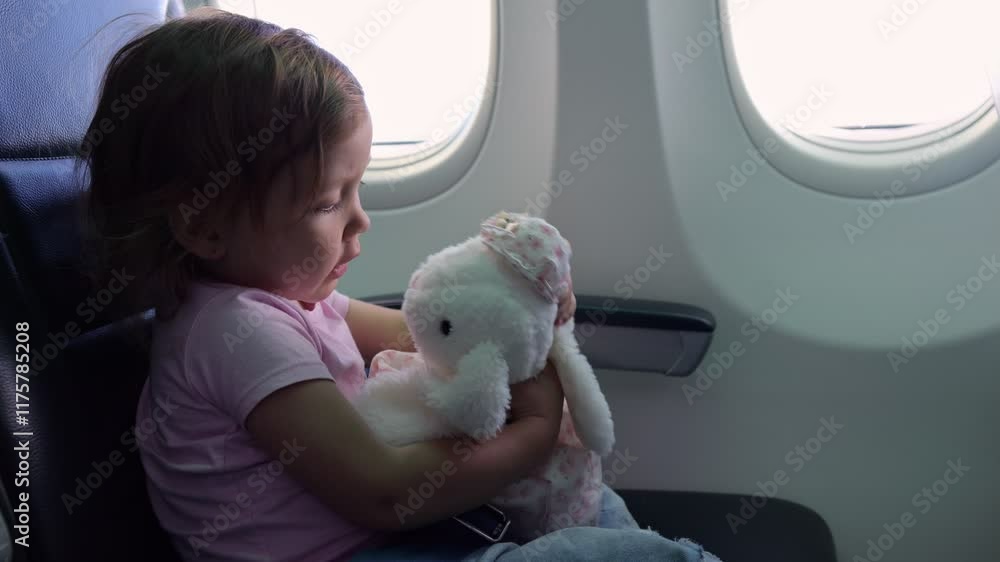 Cute blonde child hugs toy bunny sitting in airplane seat Cute blonde child hugs toy bunny sitting in airplane seat
