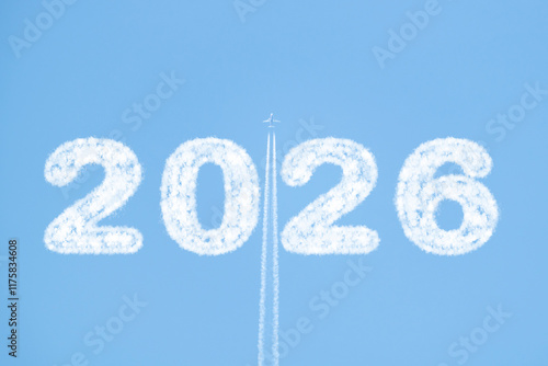 A plane flies high in a clear blue sky, trailing white smoke as it passes between clouds shaped like 