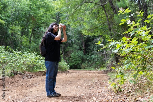 latina teenage girl with a backpack in the forest taking pictures photo