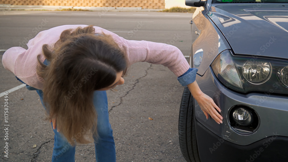 Woman examining damage on car bumper after traffic accident