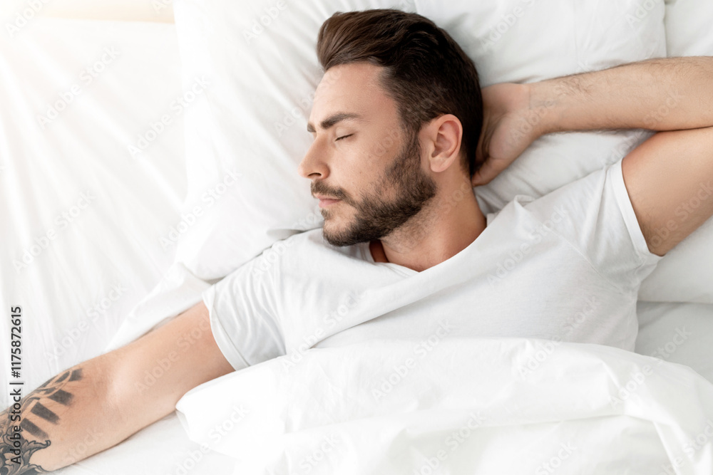 Tired millennial man sleeping, lying on white bed in bedroom, resting with eyes closed , top view, copy space. Rest, lazy, relax, sleep at home in free time on weekends Tired millennial man sleeping, lying on white bed in bedroom, resting with eyes closed , top view, copy space. Rest, lazy, relax, sleep at home in free time on weekends