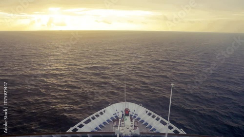 Bow of cruise ship moving over waves toward sunrise.