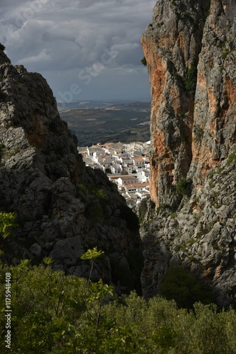 View at beautiful Zahara de la Sierra, Spain, white village clipped by limestone cliffs from nearby Garganta Verde canyon, endless hills of olive groves and captivating storm cloud sky in the distance