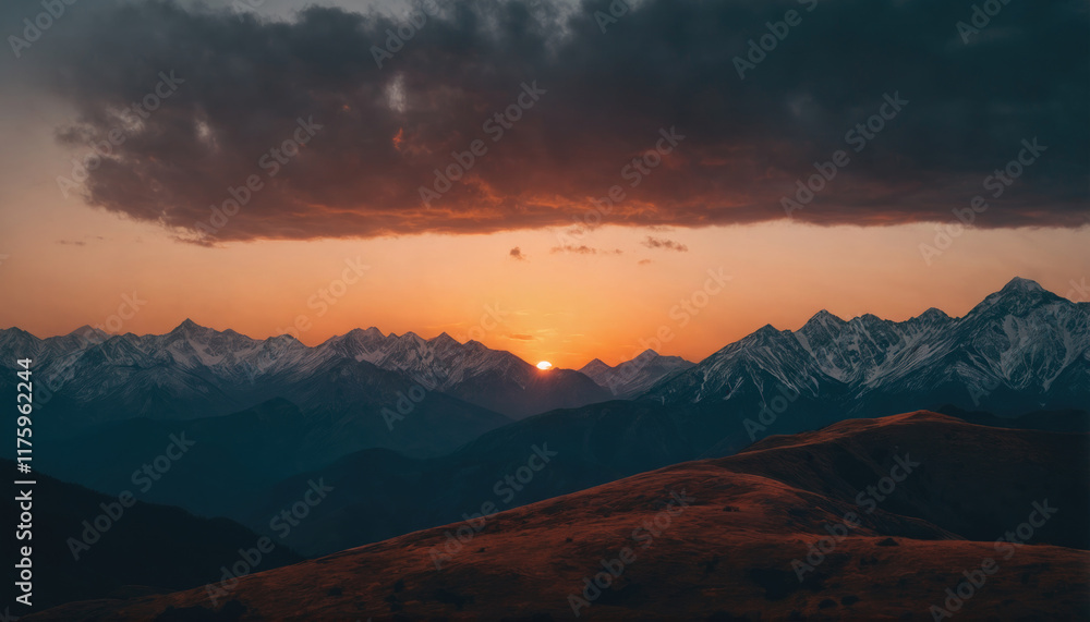Sunset over majestic mountain range with rolling hills in the foreground and dark clouds above during late evening hours Sunset over majestic mountain range with rolling hills in the foreground and dark clouds above during late evening hours