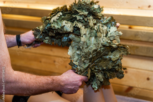 A masseur in a Russian sauna massages a young woman's legs with an oak broom. Relaxing atmosphere in the steam room of the Finnish sauna.