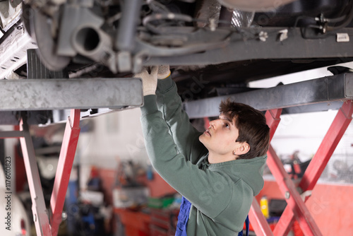 Принти на полотні Skilled focused young mechanic in warm olive hoodie and blue overalls engaged in