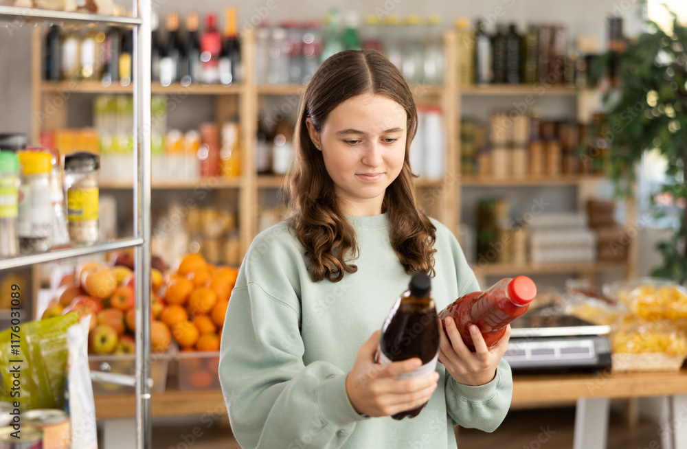 Teen girl hold packages bottles and choose consider juice in store. Market visitor choose consider make choice bottle fruit drink. Buyer pick up set of groceries for week. Teen girl hold packages bottles and choose consider juice in store. Market visitor choose consider make choice bottle fruit drink. Buyer pick up set of groceries for week.