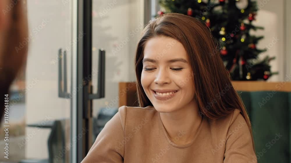A young woman engages in conversation while seated at a table in a cafe adorned with festive decorations. The warm atmosphere adds to the lively interaction taking place. A young woman engages in conversation while seated at a table in a cafe adorned with festive decorations. The warm atmosphere adds to the lively interaction taking place.