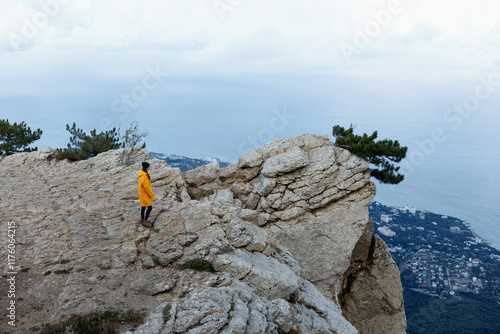 A person in a yellow jacket standing on a cliff admiring breathtaking views of a tranquil body of water and majestic mountain range photo