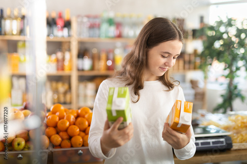 Fotografi Teenage girl buyer chooses packaged peach and apple juices in grocery store