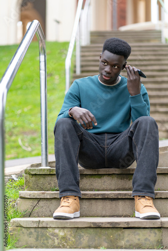 Fotografie Pensive young man listening to voicemail message while sitting on steps