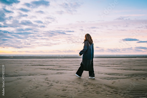 Women walking across the beach wearing a coat during sunset