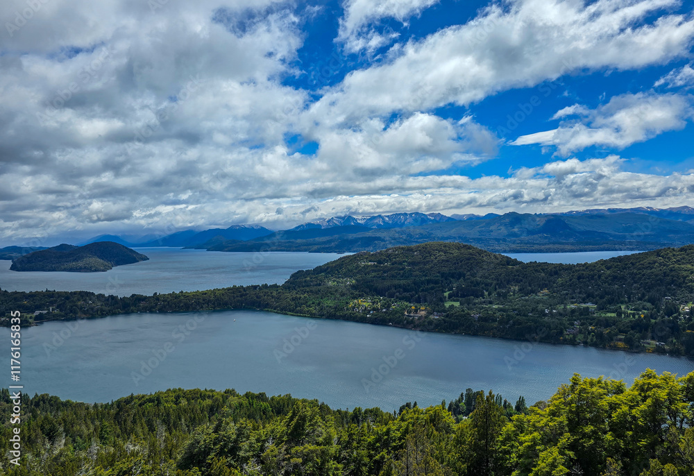 Fototapeta premium Aerial View of Lakes Surrounded by Green Hills and Distant Mountains Under a Bright Blue Sky with Puffy White Clouds