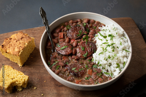 CLASSIC RED BEANS AND RICE WITH ANDOUILLE SAUSAGE, CILANTRO AND CORNBREAD ON A WOODEN BOARD WITH SPOON photo