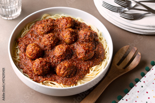 READY TO SERVE FAMILY-STYLE SPAGHETTI AND MEATBALLS  WITH A STACK OF PLATES AND FORKS photo